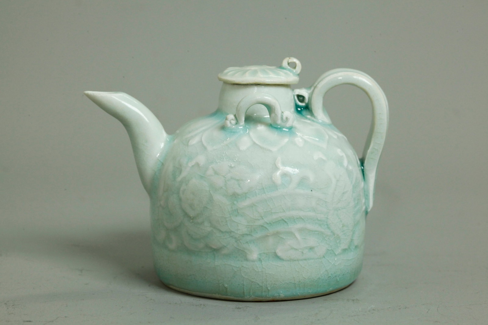Chinese Pale Blue Qingbai Porcelain Ewer: Chinese Pale Blue Qingbai crackle glazed Porcelain Ewer with each side carved and molded with a small Boy and Lotus, with Lotus Petal border to shoulders, an applied curved spout and strap handle with