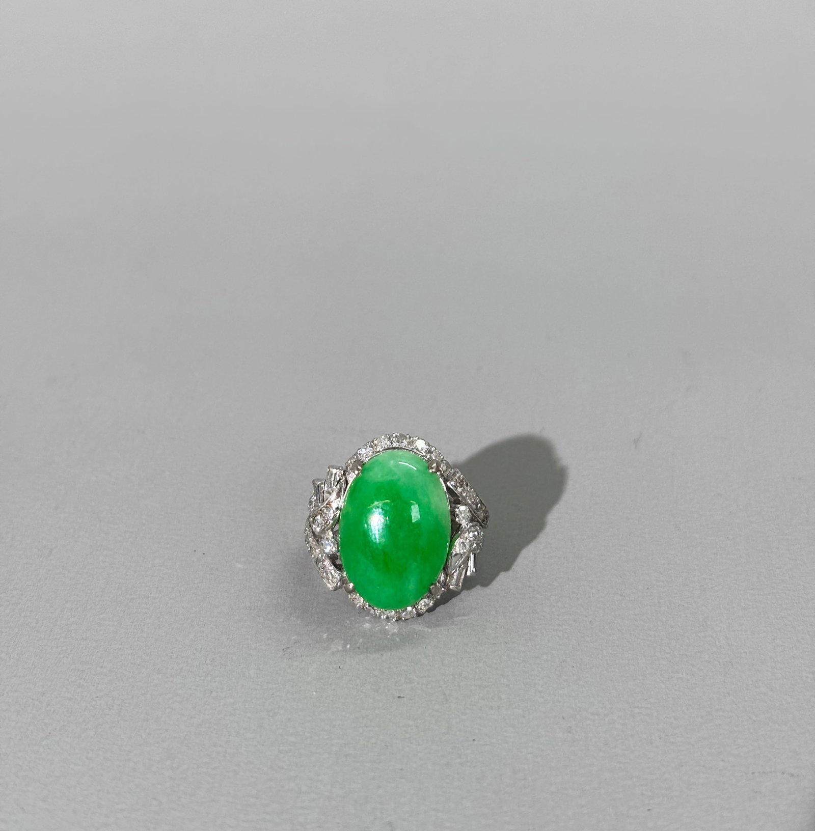 Chinese Apple Green Oval Jadeite Diamond 18K Ring: Chinese prong set translucent Apple Green Oval Cabochon Jadeite Ring in white gold marked "18K" inside band, the setting with numerous small Diamonds 4 of which are baguettes. US ring size with metal 