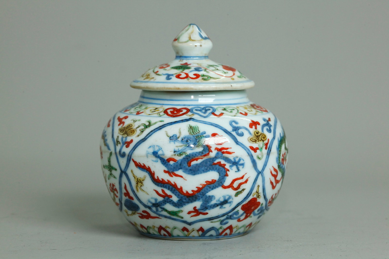 Sm Chinese Wucai Porcelain Covered Dragon Jar: Small Chinese Wucai Porcelain Covered Dragon Jar, the body with 4 quatrefoil panels each with 5-claw Dragon between Ruyi head border at shoulder and leaf border at base, the cover with scrolling Lingz