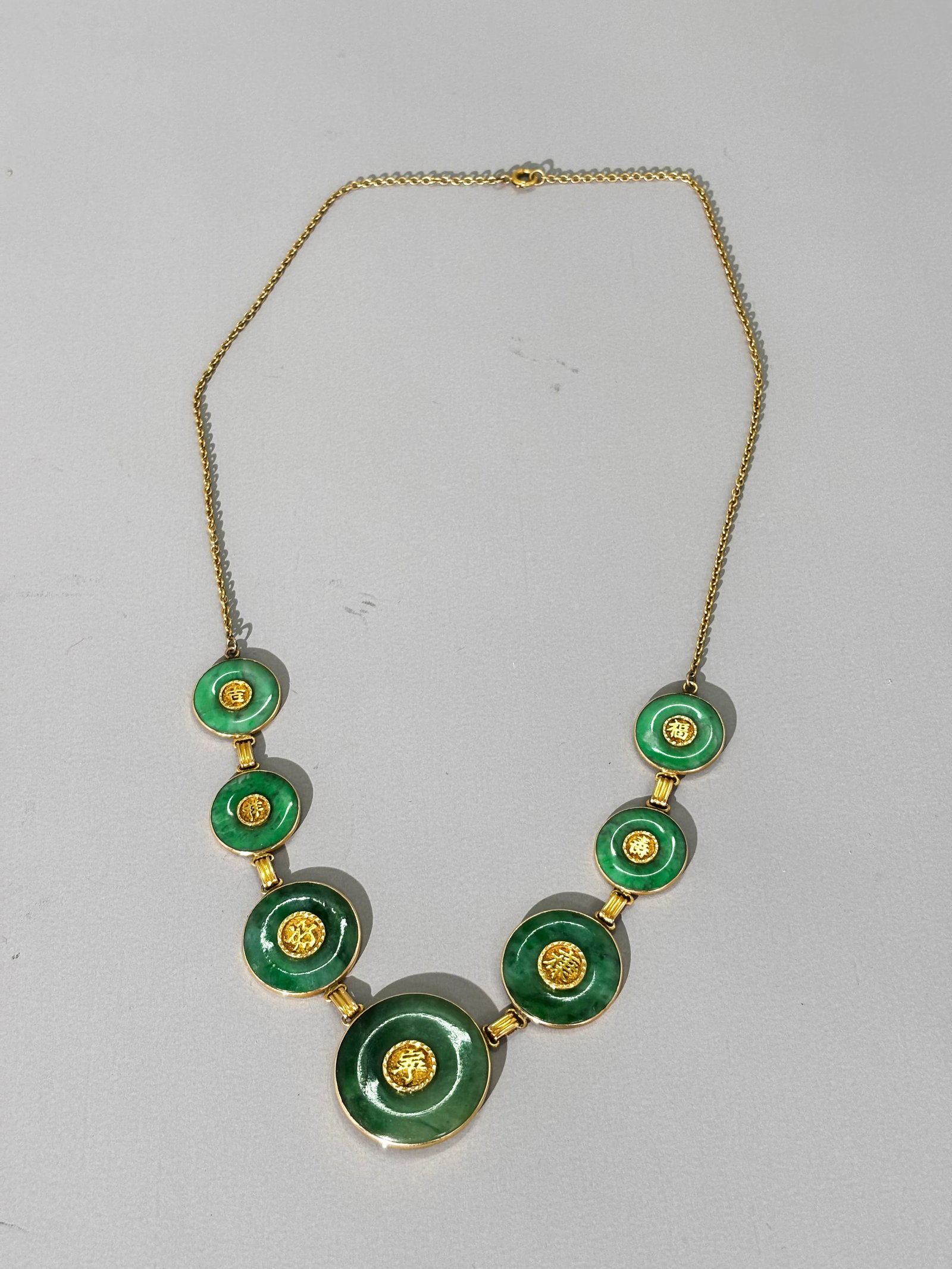 Chinese Green Jadeite & 14K Gold Necklace; 18.7G: Chinese Necklace with 7 graduated translucent Green Jadeite "Bi" Rings, each set with a yellow gold calligraphy to center hole and yellow gold bezel set with sealed yellow gold links and a yellow gold
