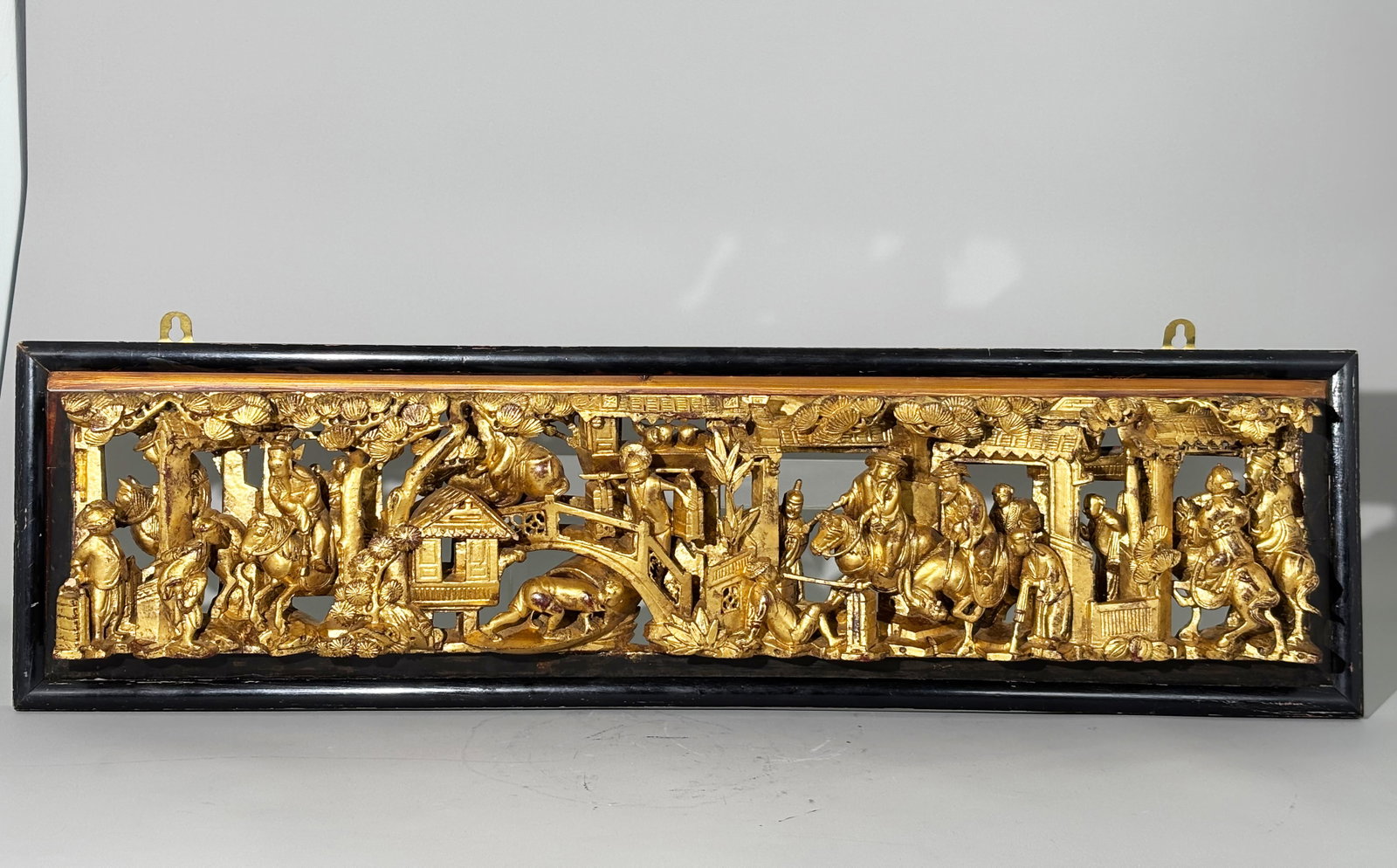 Chinese Gold Lacquer Carved Wood Horizontal Panel: Chinese Gold Lacquered Wood Horizontal Panel well carved in high relief with Mandarin Figures on Horseback moving in and around a busy town street with workers carrying packages on foot, loafers resti