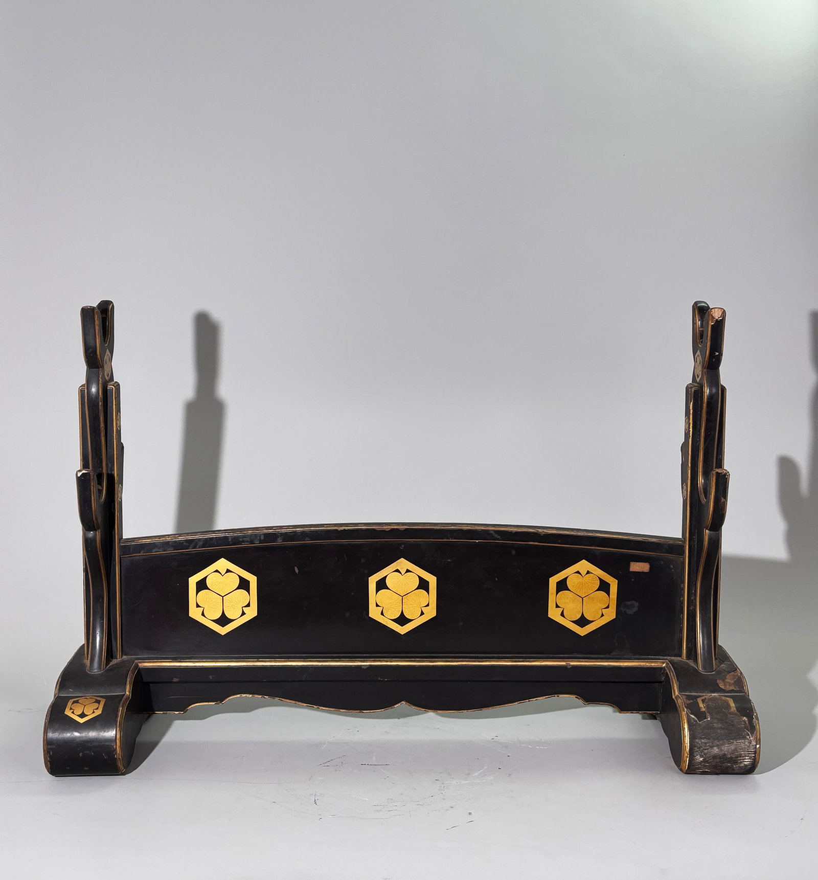 Japanese black lacquered sword stand, Meiji period: Japanese black lacquered wood sword stand (katana-kake), Meiji period. Constructed in lacquered timber, fitted with two stylised bifurcated upright supports. Decorated with gilt painted hexagonal pane