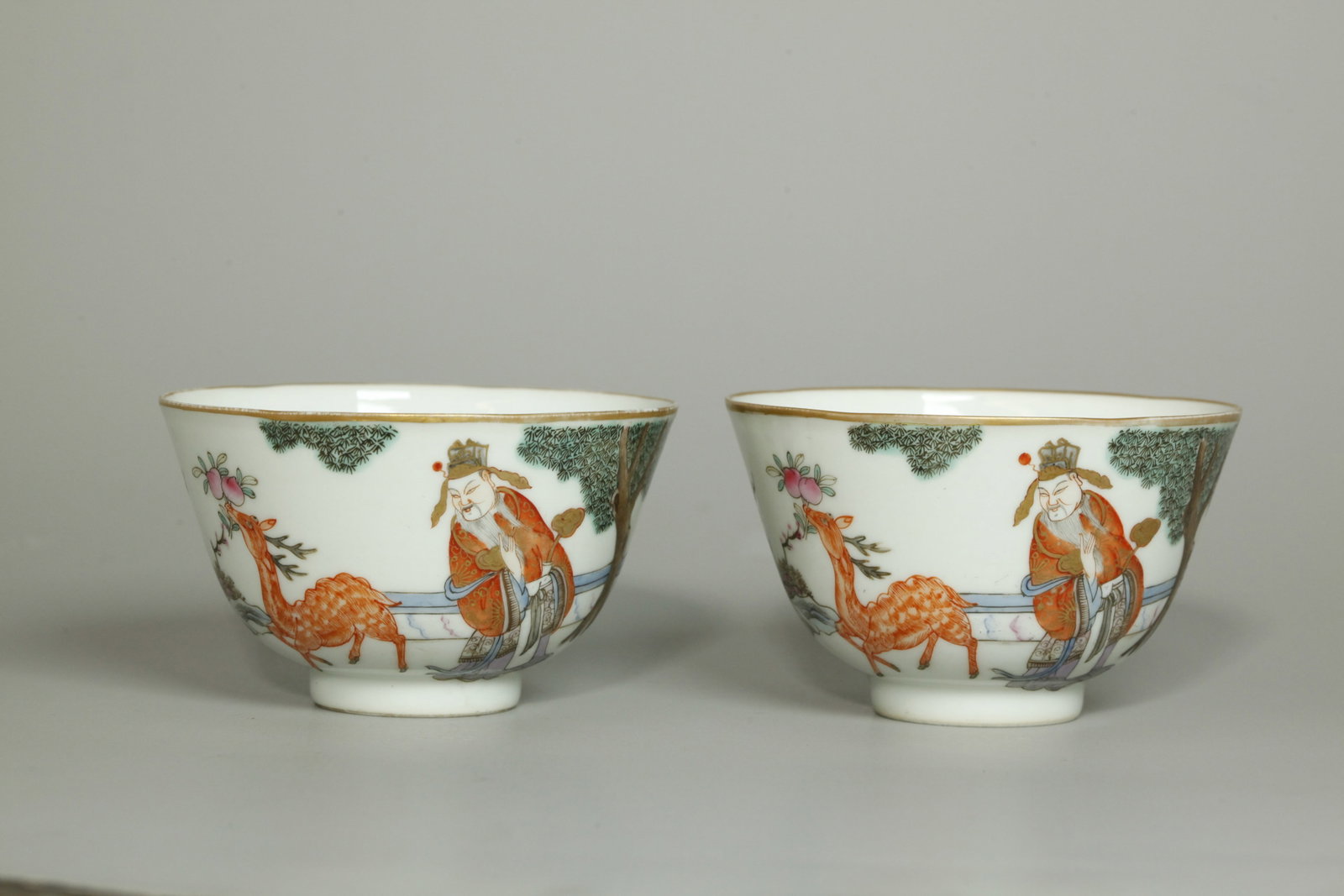 Fine Pr Chinese Qing Enameled Porcelain Teacups: Fine Pair Chinese Porcelain Teacups each well enameled with an Official, probably the Star God of Happiness, Fuxing with gilt Ruyi Scepter under a Pine Tree in Garden with Deer holding Peaches of Immo