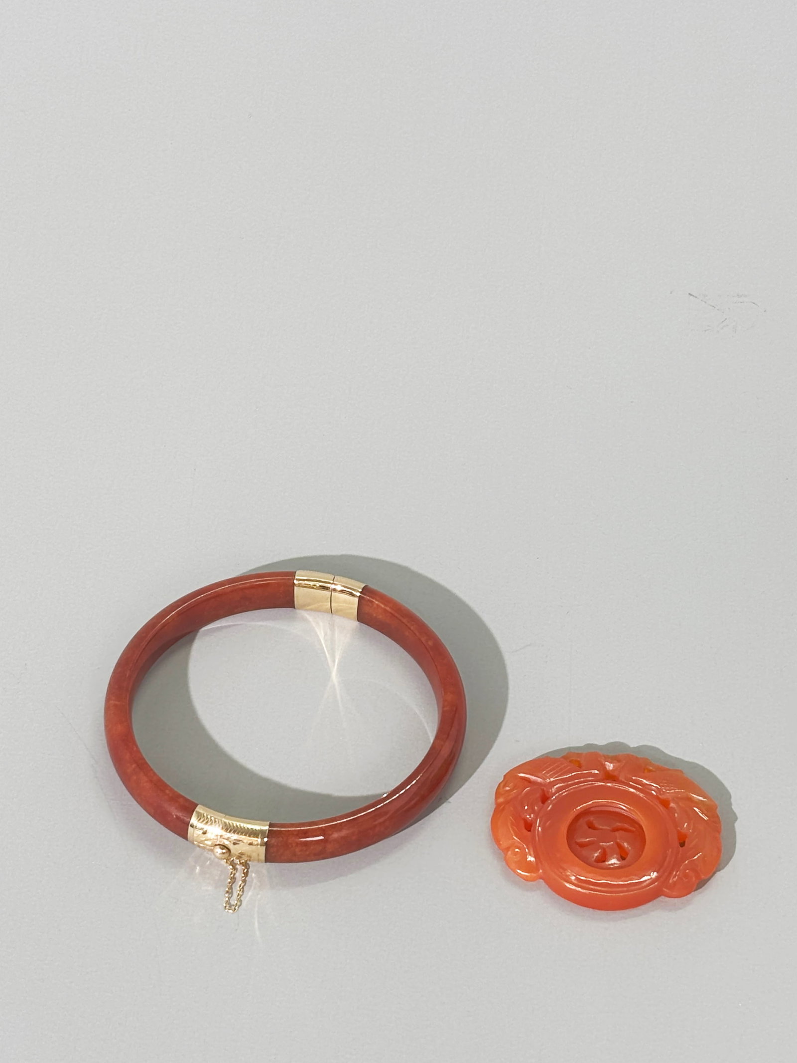 Chinese Red Jadeite 14K Bangle Carnelian Pendant: Chinese Russet Red Jadeite Bangle hinged in yellow gold marked "14K/585" at closure with safety chain; together with a Carnelian Agate Spinner Pendant with loose integral round ring below double Phoen