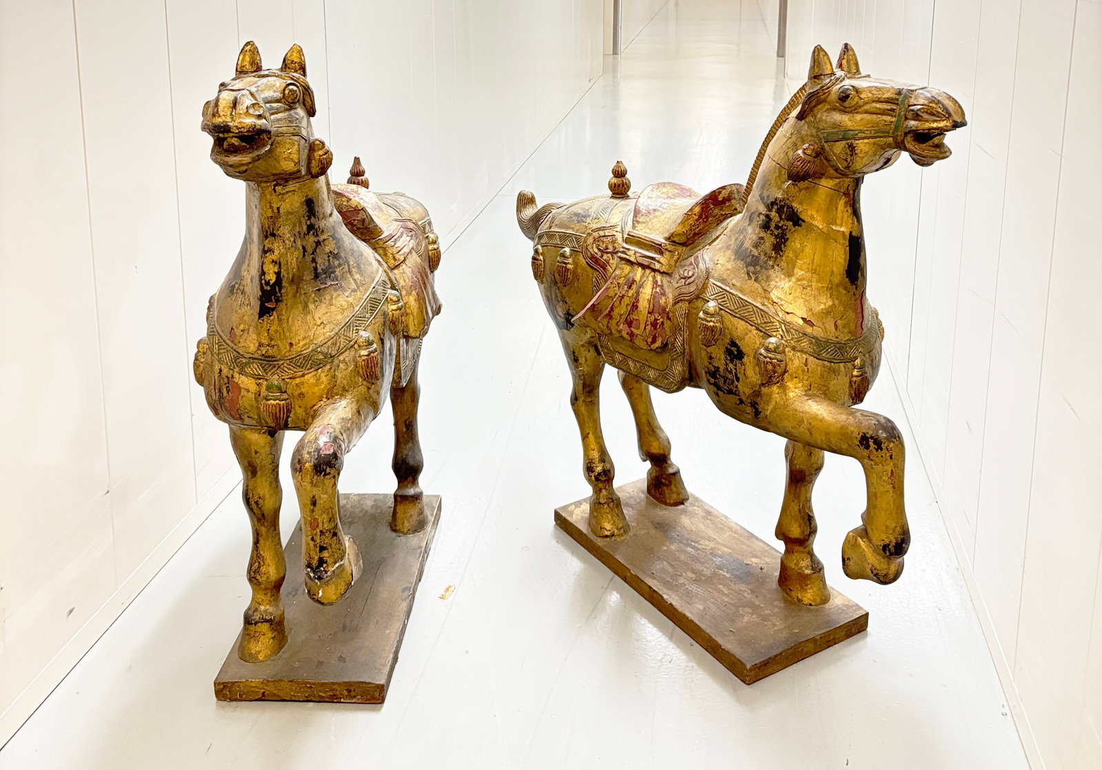 Lg Mirror Pair Chinese Carved & Gilt Wood Horses: Large Mirror Pair Chinese Carved & Gilt Wood Horses, each standing on 3 legs on a rectangular platform with alternate raised front hoof; with saddles and horse tack including tassels. Height 41 3/4' i