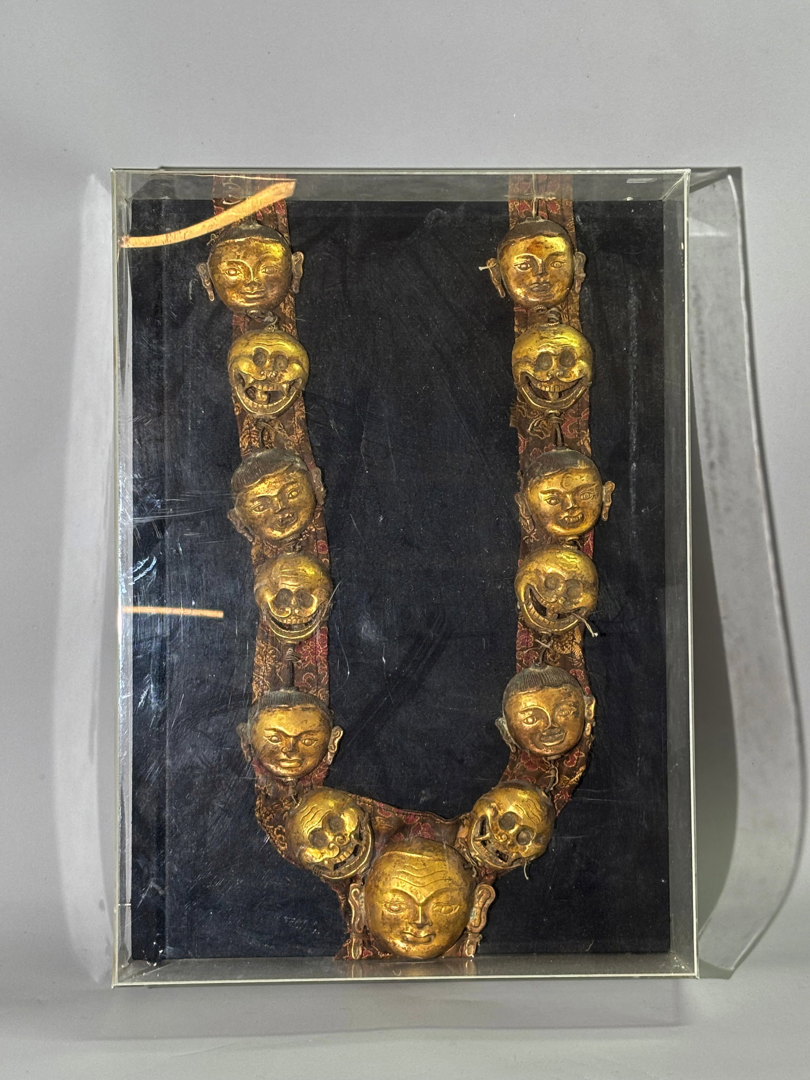 Tibetan Gilt Bronze Mahakala Ritual Scull Necklace: Tibetan Gilt Bronze Mahakala Ritual Necklace with 13 Sculls and the Heads of Vanquished Demons each separate and with finely incised details, attached to old brocade; used for the year-end Grand Puja 