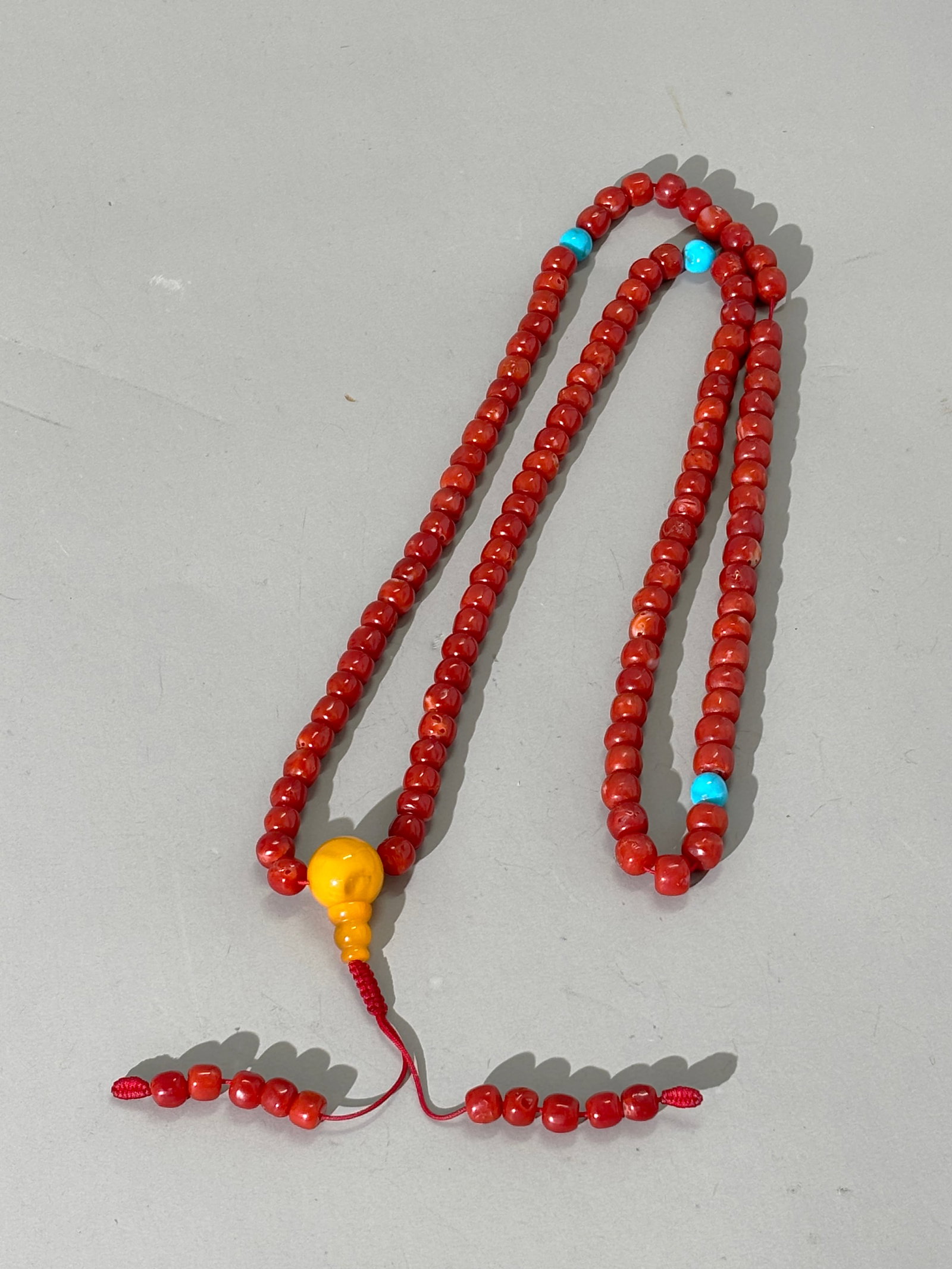 Tibetan 108 Bead Dark Coral Buddhist Rosary; 74G: Tibetan 108 Bead Dark Coral Buddhist Rosary with 3 small turquoise spacer beads, an amber head bead and 10 small coral tassels. Total weight 74 grams. Length 29 inches.