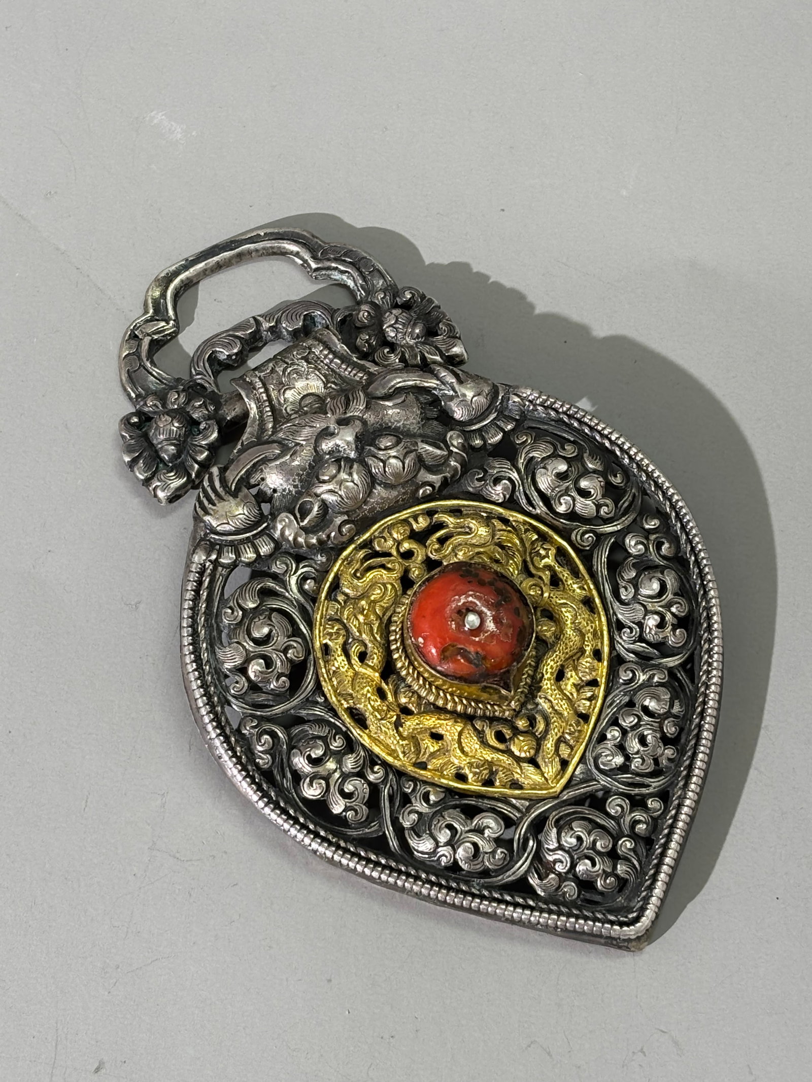 Tibetan Silver & Gilt Chupa Belt Ornament; 88.5G: Tibetan Silver & Gilt Metal Chupa Belt Ornament formed as a large incised & pierced silver petal shape inlaid to center with gilt metal and a coral, with additional silver loose loop end, worn attache