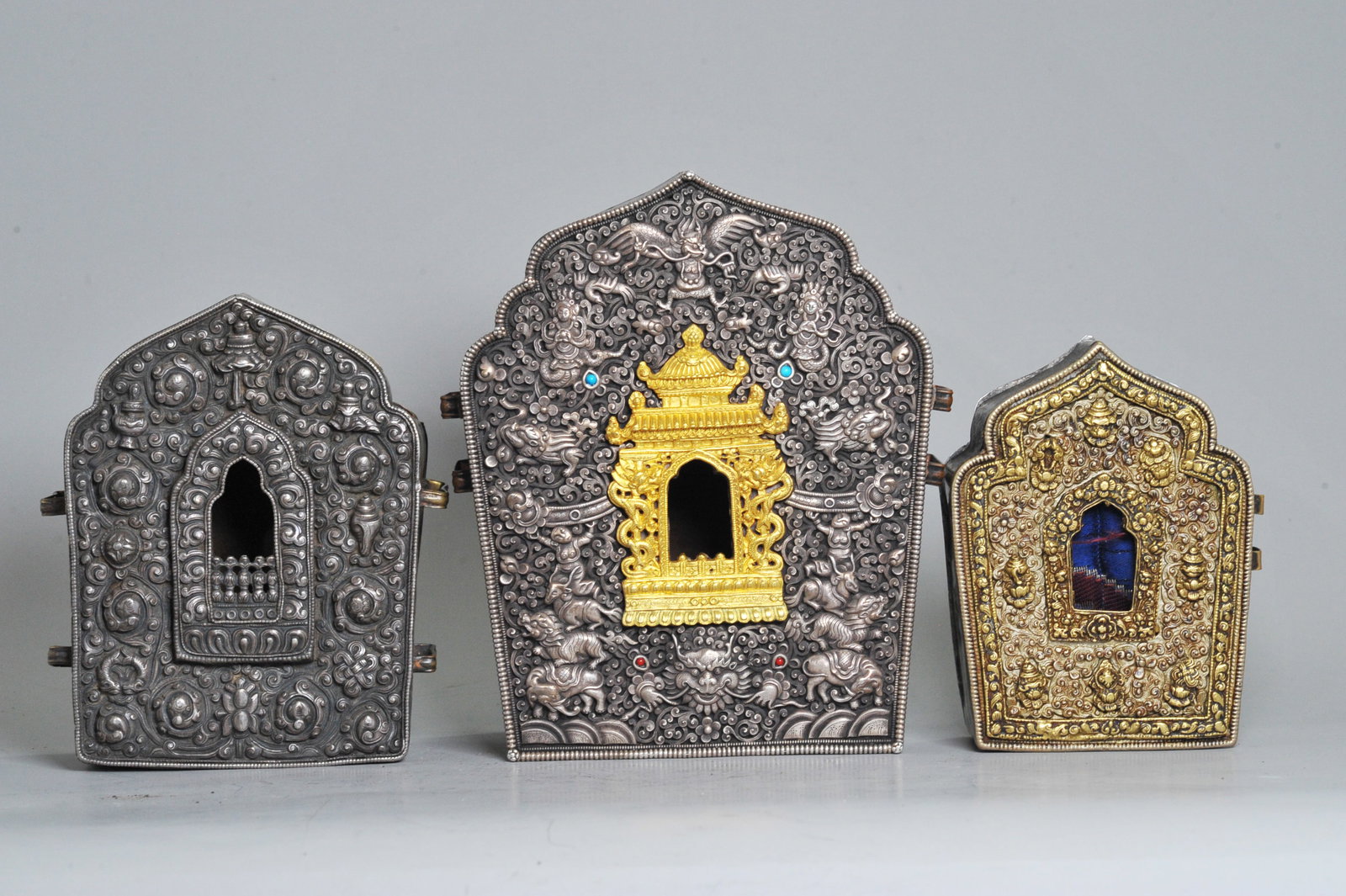 3 Good Tibetan Gao Devotional Boxes: 3 Good Tibetan Gao Devotional Boxes each with strap handles to sides and opening in the back: the largest with an incised silver & gilt front with Garuda to top and Figures with Sacred Animals to side