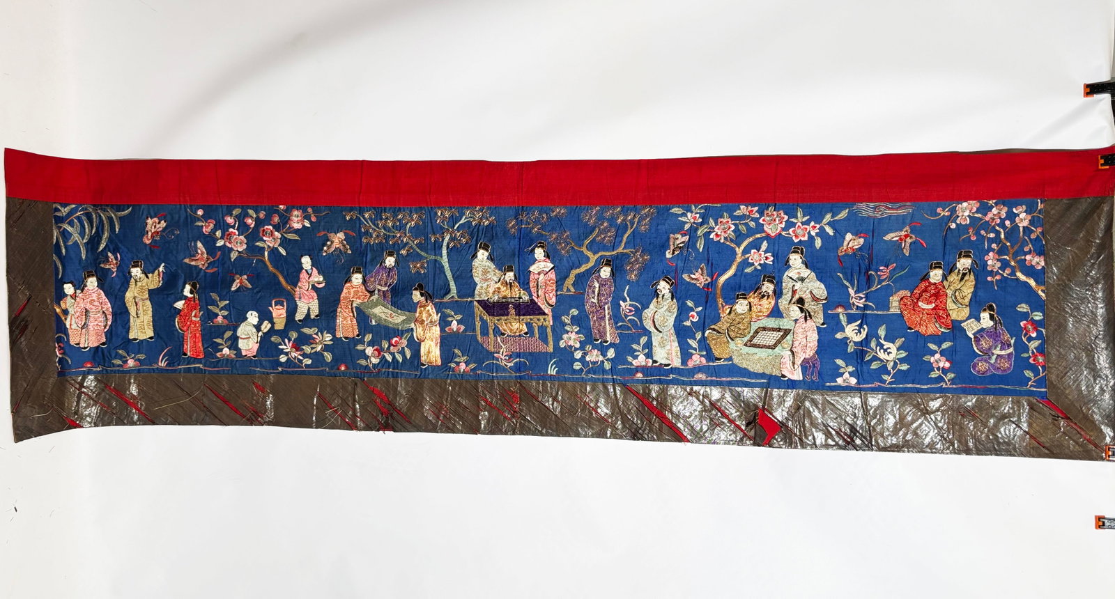 Chinese 19th C 18 Scholars Gold & Blue Silk Panel: Chinese 19th Century laid gold wrapped thread & colored silks, with a design of a meeting of 18 Scholars with assistants in a Flower Garden on a Blue Silk horizontal Panel, the top edge with a red fab