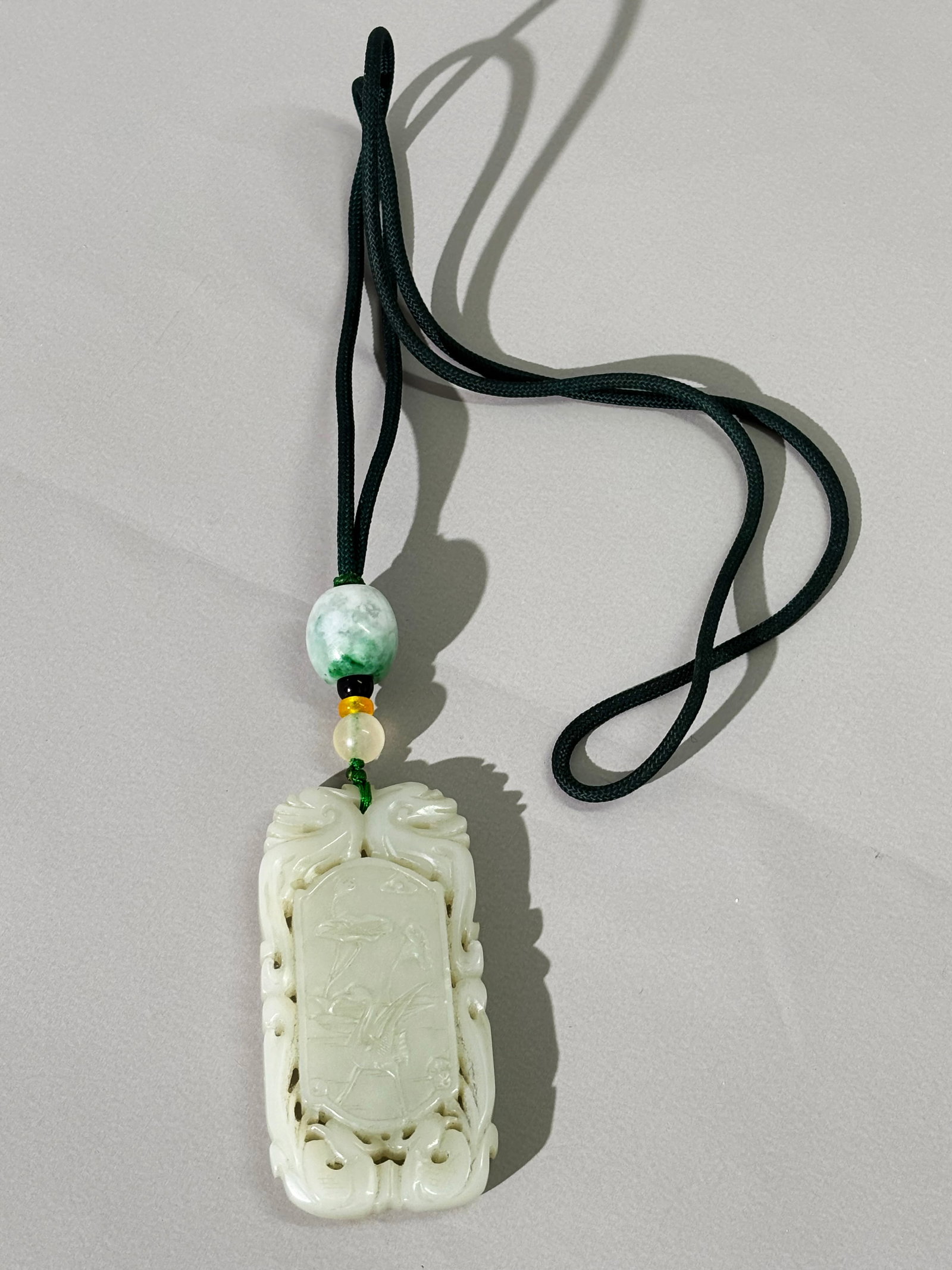 Chinese Carved Celadon Jade Pendant: Chinese Carved Celadon Jade Pendant. Rectangular white jade pendant with open-carved dragon-form border. One side carved with crane and lotus, reverse depicting landscape with figure on boat. Strung w