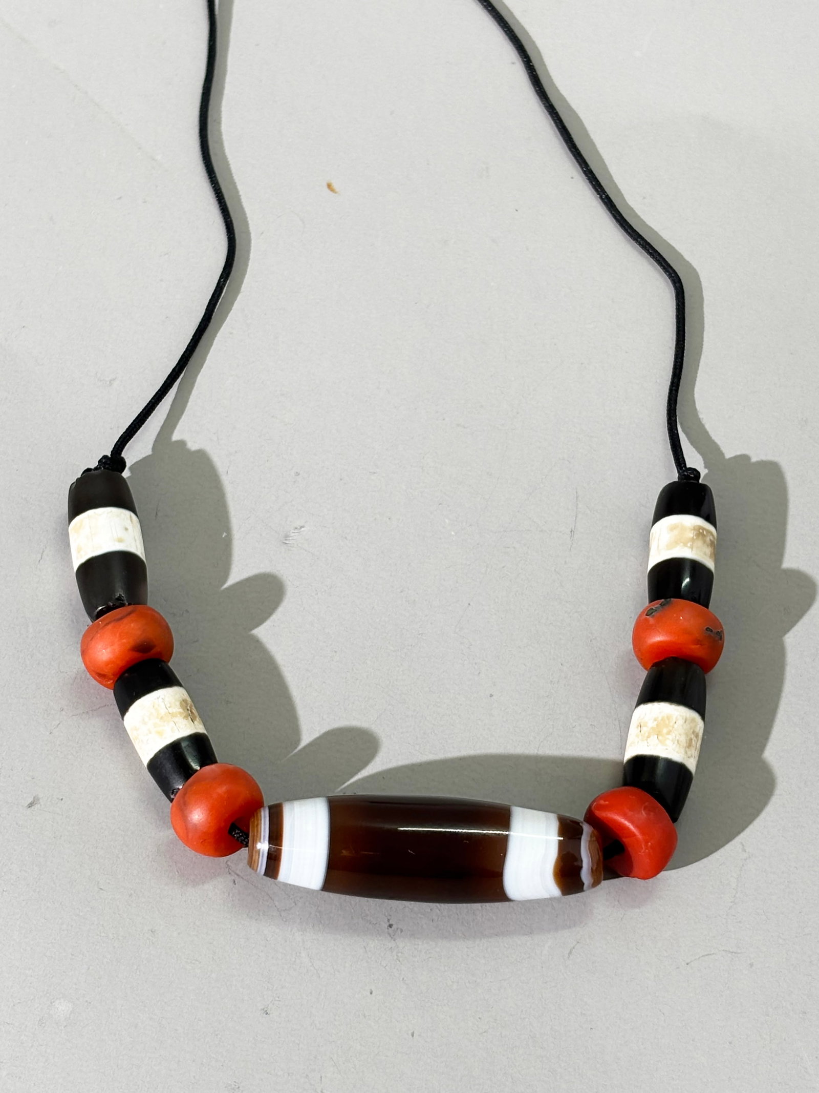 5 Tibetan Dzi Beads, 1 Long and 4 Short; 36G: 5 Tibetan Dzi Beads, 1 Long and 4 Short, strung on cord with 4 coral beads.; Total weight 36 grams. Length of long bead 1 3/4 inches.