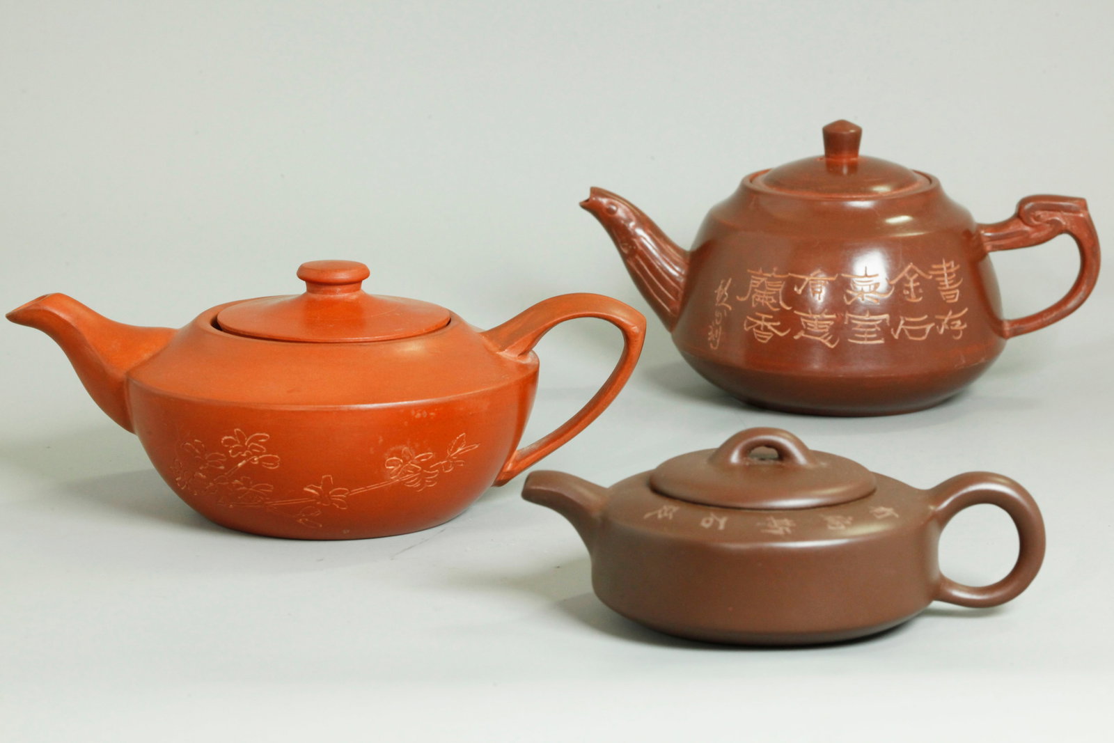 3 Chinese Yixing Zisha Teapots 2 Polished Outside: 3 Chinese Yixing Zisha Teapots; the largest in light red clay with outside polishing, inside loose tea infuser, incised flowers and calligraphy to the sides and an impressed "Made in China" mark to bo