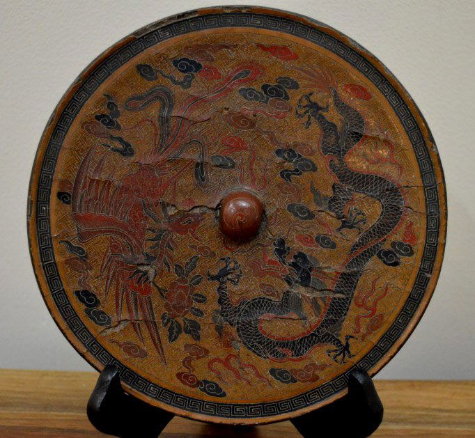 Chinese Cinnabar Lacquer over Bronze Mirror: Chinese Cinnabar Lacquer over bronze mirror, the lacquer carved with phoenix and dragon. age related cracks and losses to lacquer, bronze corrosion. Dia: 7 1/2 inches (19cm).
