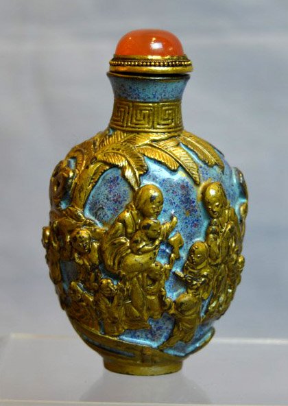 Chinese Porcelain Snuff Bottle: Chinese Porcelain Snuff Bottle with bronze top set with carnelian, the bottle molded with figures and glazed with robins egg and gold to imitate ancient bronze. Height including cover 3 inches (8 cm.)