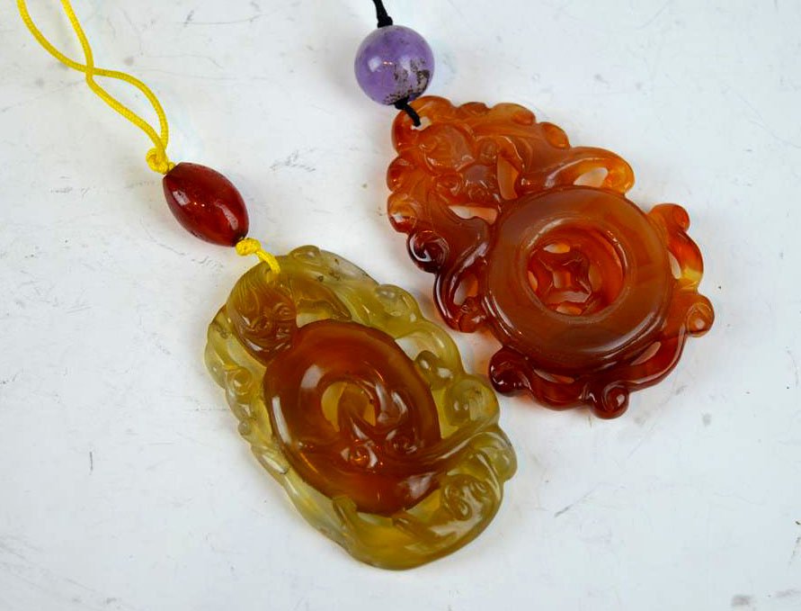2 Chinese Carved Agate Pendants: 2 Chinese Carved Agate Pendants. One with a dragon with restored breaks to one edge; One Carnelian with a revolving center with a chip. Length of larger 2 1/4 inches (6 cm.).