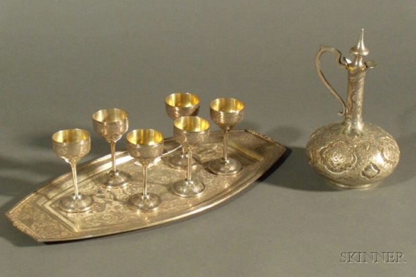 Eight Piece Middle Eastern Silver Cordial Set, ear: Eight Piece Middle Eastern Silver Cordial Set, early 20th century, Iran, comprising an ovoid decanter with slender neck and tapering stopper, ht. 8, a boat shaped tray, lg. 14 7/8, and set of six foot