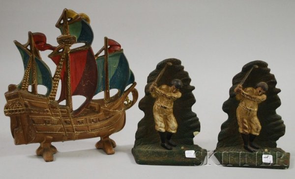 Three Polychrome Metal Decorative Items, a ship-fo: Three Polychrome Metal Decorative Items, a ship-form doorstop and a pair of golfer bookends, (some minor paint cracking and loss).