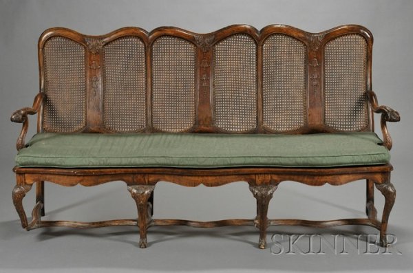 Queen Anne Walnut and Caned Seat Settee, early 18th: Queen Anne Walnut and Caned Seat Settee, early 18th century, with serpentine backrest carved with foliage, scrolled arms, loose cushion and caned seat, on foliate carved cabriole legs joined by stretc