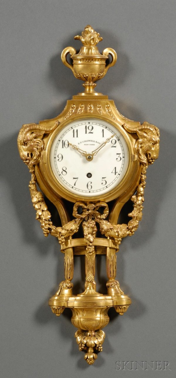 Neoclassical Gilt-brass Cartel Clock by Chelsea, t: Neoclassical Gilt-brass Cartel Clock by Chelsea, the cast brass case with urn surmounting the 4 1/4 in. porcelain dial marked E. F. Caldwell & Co., New York, flanked by animal figure heads and garland