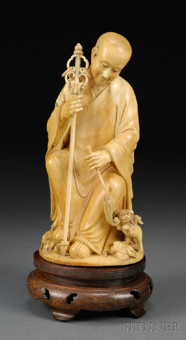 Ivory Carving, China, 19th century, carved as a se: Ivory Carving, China, 19th century, carved as a seated Luohan holding a lance in his right hand and a whisk in his left, the end of which is held by a foo dog, wood stand, ht. 7 1/2 in.