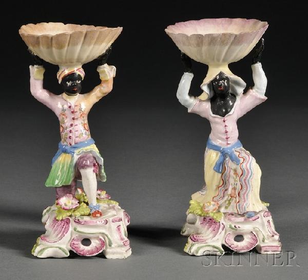 Pair of French Hard Paste Porcelain Figural "Black: Pair of French Hard Paste Porcelain Figural "Blackamoor" Salt Cellars, mid-late 19th century, formed as a male and a female kneeling Moor in 18th century dress, each holding aloft and ovoid open salt