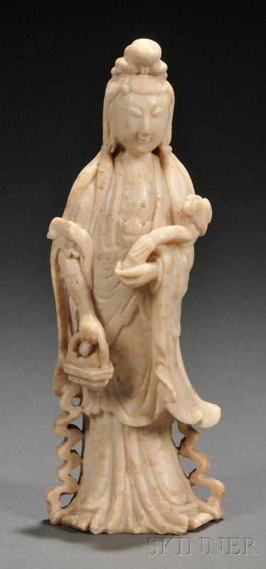 Soapstone Carving, China, figure of Guanyin holdin: Soapstone Carving, China, figure of Guanyin holding a lingzhi sprig in her left hand and a flower basket in her right, dark soapstone stand, ht. 9 3/8, 11 in. (with stand).