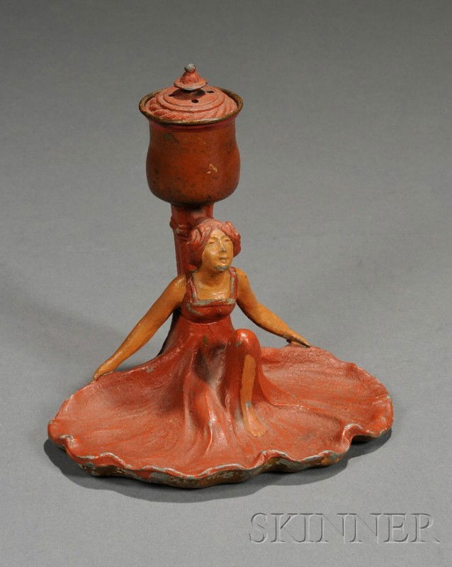 Art Nouveau Figural Inkwell Painted cast metal Lat: Art Nouveau Figural Inkwell Painted cast metal Late 19th/early 20th century Cast in the form of a woman in a flowing dress, covered inkwell, lacking glass insert, paint losses, ht. 4 3/4, wd. 5, dp. 4