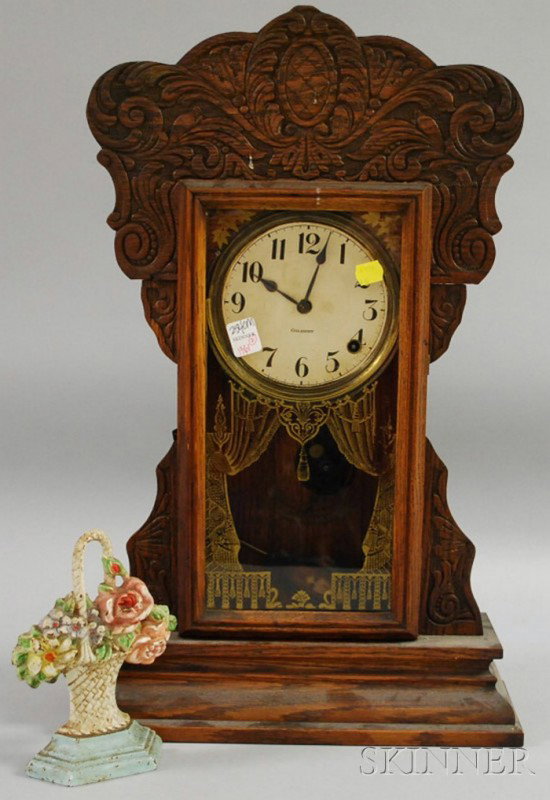 Gilbert Capitol No. 44 Pressed Oak Gingerbread Sh: Gilbert Capitol No. 44 Pressed Oak Gingerbread Shelf Clock and a Painted Cast Iron Basket of Flowers Doorstop, the clock with brass spring-powered movement, replaced pendulum, (lacking winder/key).