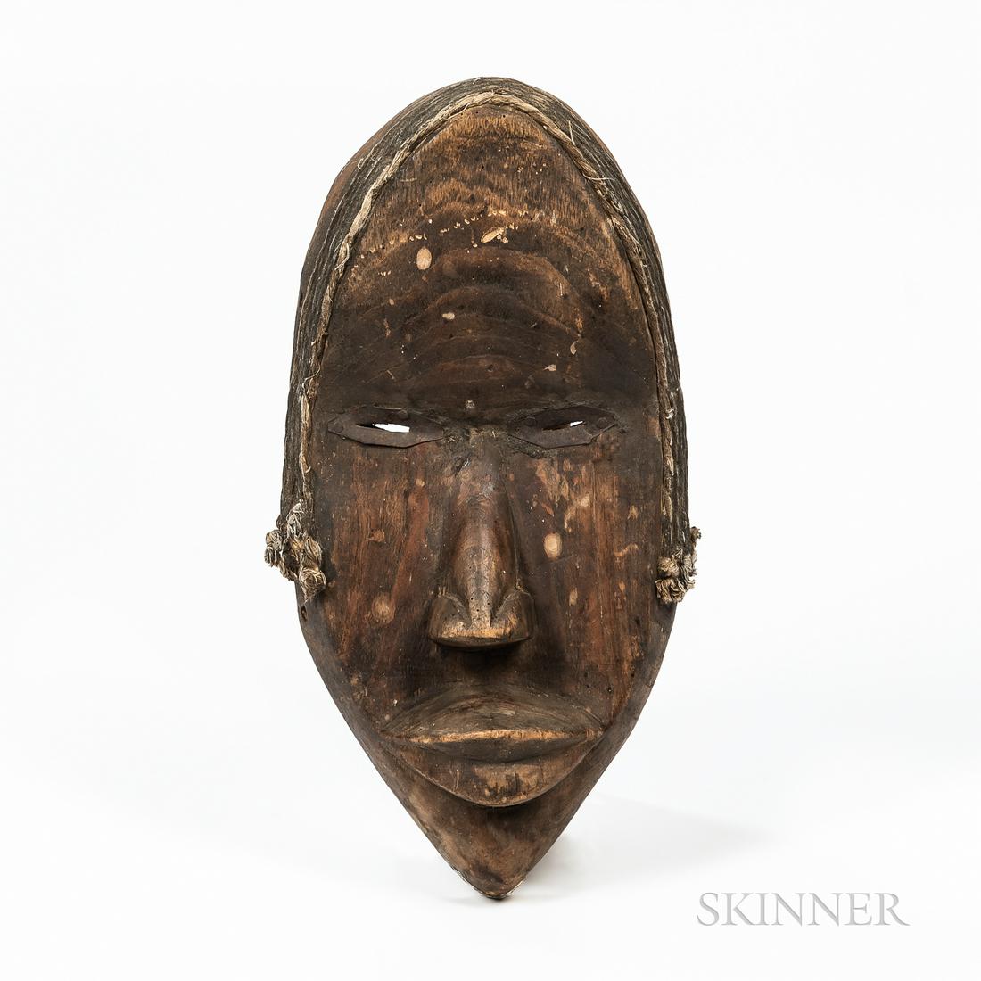 Dan Mask, hollowed-out form, pierced in the rim, with full protruding lips, triangular nose, narrow: Dan Mask, hollowed-out form, pierced in the rim, with full protruding lips, triangular nose, narrow slit eyes, with metal surrounds, under a high forehead, with fiber attached around top and sides, ht