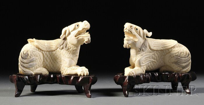 Pair of Ivory Carvings, China, early 20th century,: Pair of Ivory Carvings, China, early 20th century, a pair of mythical animals with dragon heads, bird's wings, and lion's paws, wood stands, lg. 4 3/4 in.