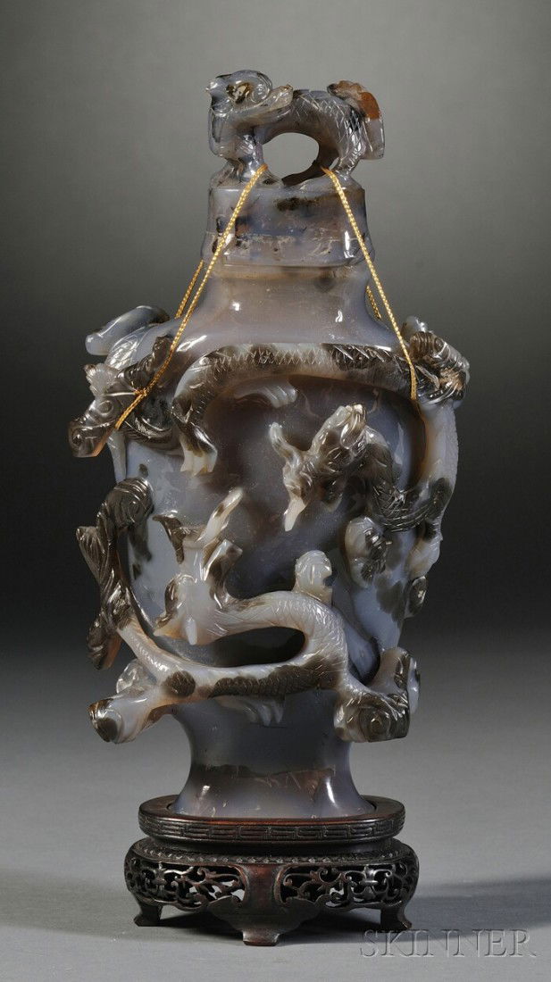 Agate Covered Vase, China, the hu-shaped body wra: Agate Covered Vase, China, the hu-shaped body wrapped with relief carving of dragons, domed cover surmounted by a foo dog, wood stand, ht. 9 1/4 in.