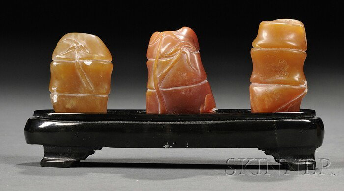 Three Soapstone Seals, China, each finely carved: Three Soapstone Seals, China, each finely carved as a bamboo shoot with reliefs of leafy sprigs, the stone of ochre, orange-red, and toffee color, wood stand, lg. to 1 1/4 in.