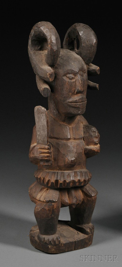Ibo Carved Wood Ikenga Figure, the standing male fo: Ibo Carved Wood Ikenga Figure, the standing male form with horn-like coiffure, with a knife in one hand and a human (?) head in the other, (wood loss), ht. 15 1/2 in.