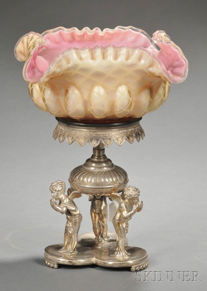 Cased Glass Bride's Basket on Stand, the basket w: Cased Glass Bride's Basket on Stand, the basket with lacy rim, yellow ground exterior with pink interior, lg. 9 1/2; set in a Derby Silver Co. silver-plated aesthetic-style base with putti supports, o