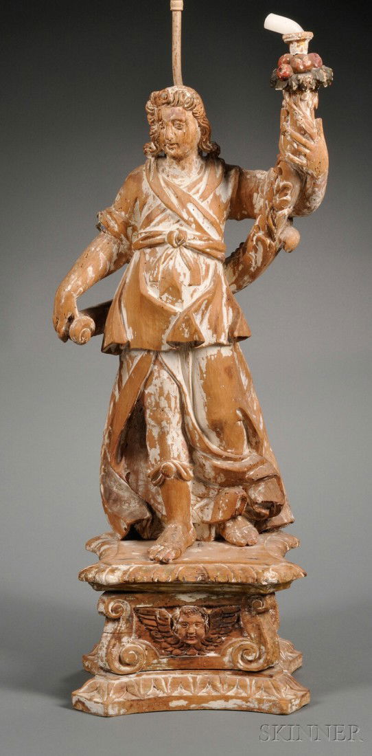 Figural Carved Limewood Lamp Base, Continental, 1: Figural Carved Limewood Lamp Base, Continental, 18th century the standing figure modeled holding a foliate and fruit decorated candle arm, and standing on an angel decorated plinth, electrified, ht. 3