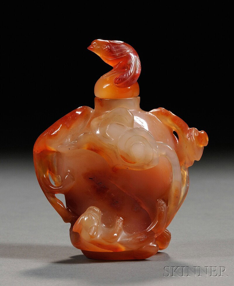 Carnelian Snuff Bottle, China, early 20th century: Carnelian Snuff Bottle, China, early 20th century, the hu-shaped body carved in high relief with chi dragons and lingzhi branches, with stopper and a bird finial, lg. 2 1/4 in.