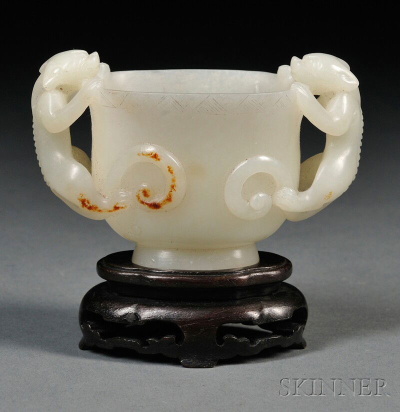 Jade Cup with Stand, China, of flattened hu shape: Jade Cup with Stand, China, of flattened hu shape, raised on a pedestal foot, flanked by chilong handles, the stone of semi-translucent pale celadon color with minor russet markings, ht. 2 1/4 in.