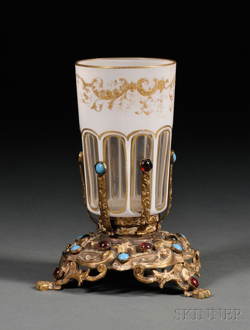 Bohemian White-cased Cut-to-clear Glass Beaker on : Bohemian White-cased Cut-to-clear Glass Beaker on "Jeweled" Gilt-metal Stand, late 19th century, the beaker panel-cut and accented with gilding, ht. 3 1/8, on pressed metal stand mounted with turquois