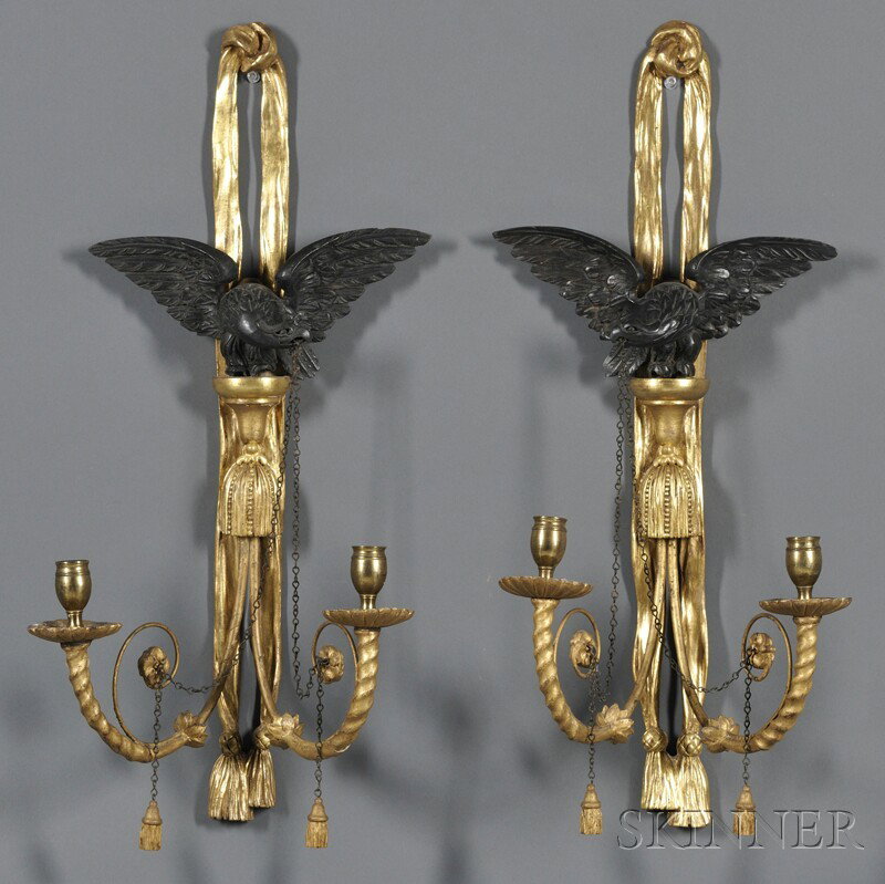 Pair of Carved Ebonized and Parcel-gilt Two-light: Pair of Carved Ebonized and Parcel-gilt Two-light Wall Sconces, America, early 20th century, each with ribband wall mount and an eagle with chains in its beak, above two scrolled candle stems, ht. 24 