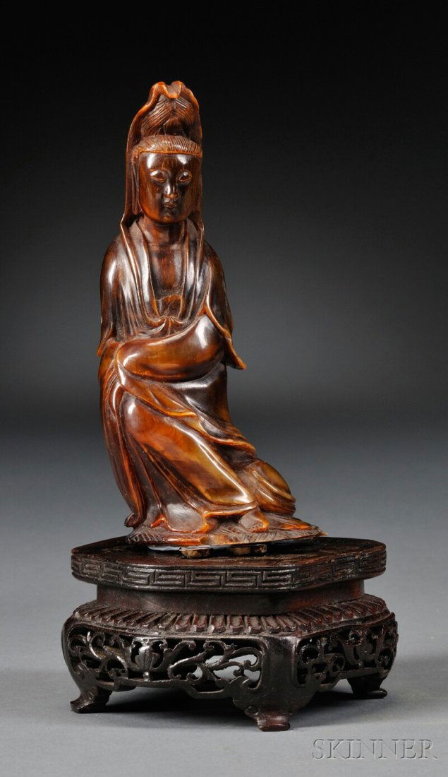 Carved Horn Kuan Yin, China, 19th century, seated on a: Carved Horn Kuan Yin, China, 19th century, seated on a lotus base with her hands folded into her robes, with carved wooden stand, ht. 5 1/2 in.