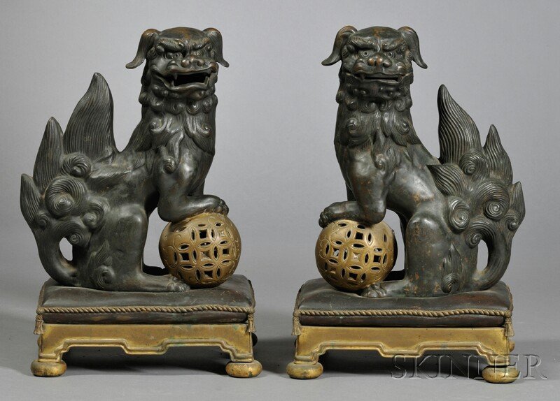 Pair of Bronze Foo Dogs, China, late 19th century, surm: Pair of Bronze Foo Dogs, China, late 19th century, surmounted on a rectangular base, each foo dog has one foot resting on a gilt brocade pierced ball, ht. 19, wd. 11 3/4 in.