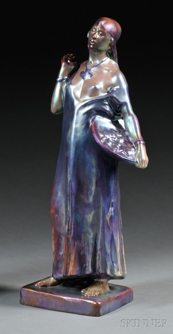 , Zsolnay "Fig Seller" Figure, Glazed ceramic, Wom: Zsolnay "Fig Seller" Figure Glazed ceramic Sculpted by Lßszl? Besz?des, Hungary, c. 1910-14 Woman in head scarf and loose dress holding a basket of figs at her side, standing on rectangular plinth in