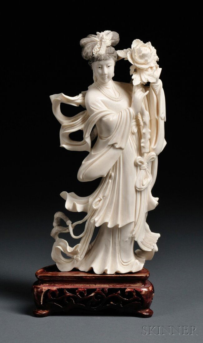 Ivory Carving on Wood Stand, China, 20th century, d: Ivory Carving on Wood Stand, China, 20th century, depicting a woman wearing long, flowing robes and holding a peony sprig in both hands above her left shoulder, ht. 9 in.