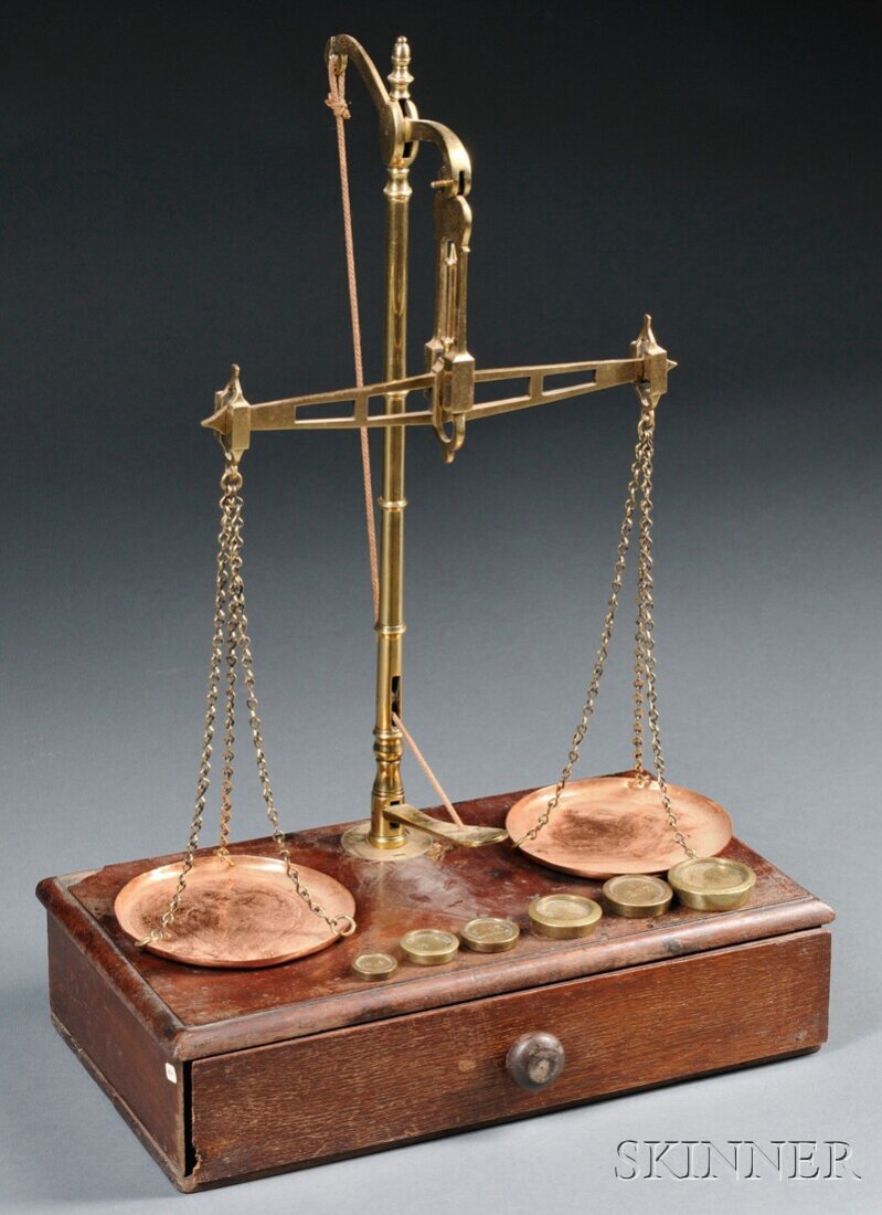 Brass and Wood Balance Scale, central column with: Brass and Wood Balance Scale, central column with height adjustment pedal and turned finial, secured to a single-drawer cabinet, pierced beam with two copper pans and chains, six weights ranging from 