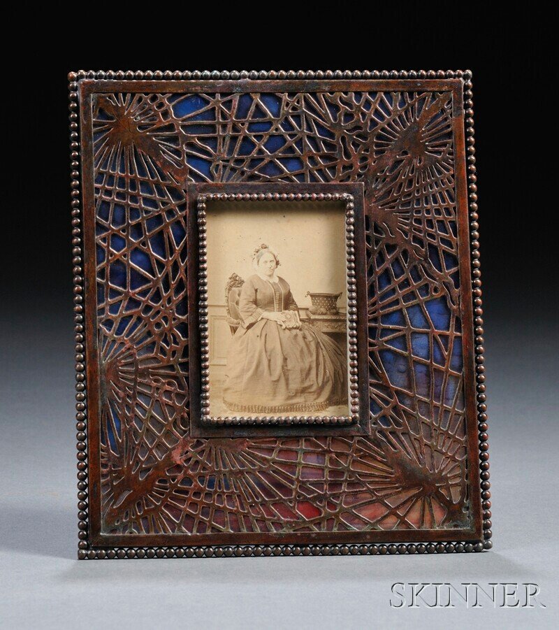 , Tiffany Studios Picture Frame, Patinated bronze a: Tiffany Studios Picture Frame Patinated bronze and art glass New York, early 20th century Pine needle metal overlay border over striated glass with beaded edge, in reddish- brown patina, fitted with a