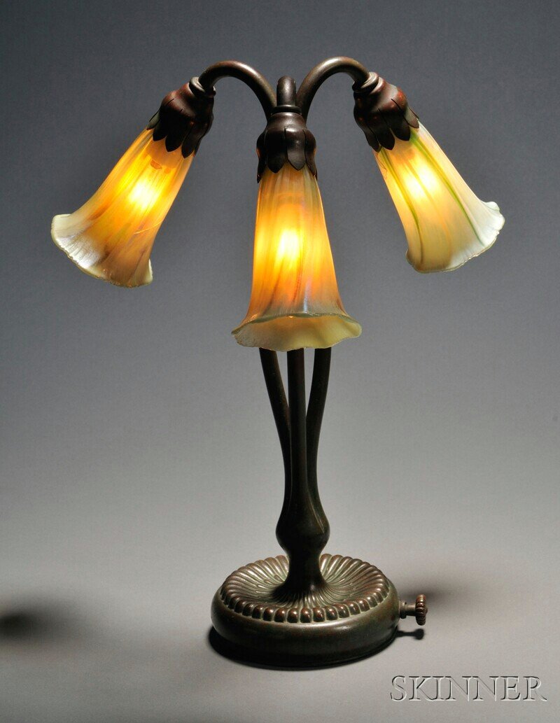 , Tiffany Studios Lily Lamp, Bronze and art glass,: Tiffany Studios Lily Lamp Bronze and art glass New York, early 20th century Three green favrile glass lily-form shades pendant from tri-form verdigris standard with circular ribbed base, marked Tiffan