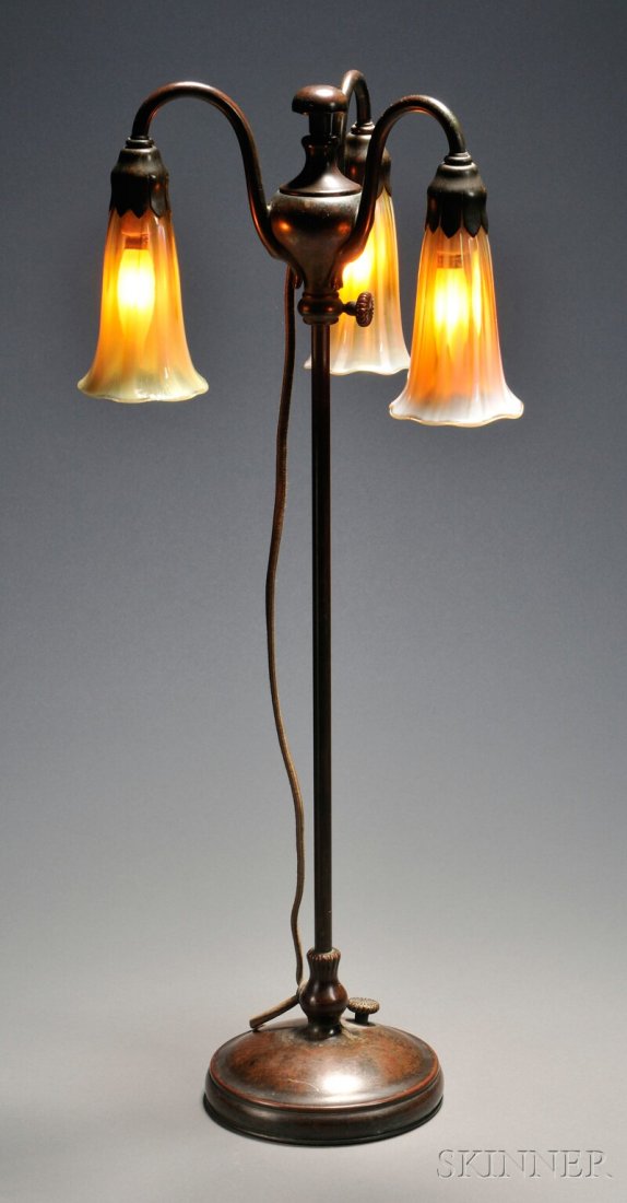 , Tiffany Studios Table Lamp, Bronze and art glass: Tiffany Studios Table Lamp Bronze and art glass New York, early 20th century Three iridescent and opalescent lily-form art glass shades, pendant from three loop arms on adjustable slender standard, ra