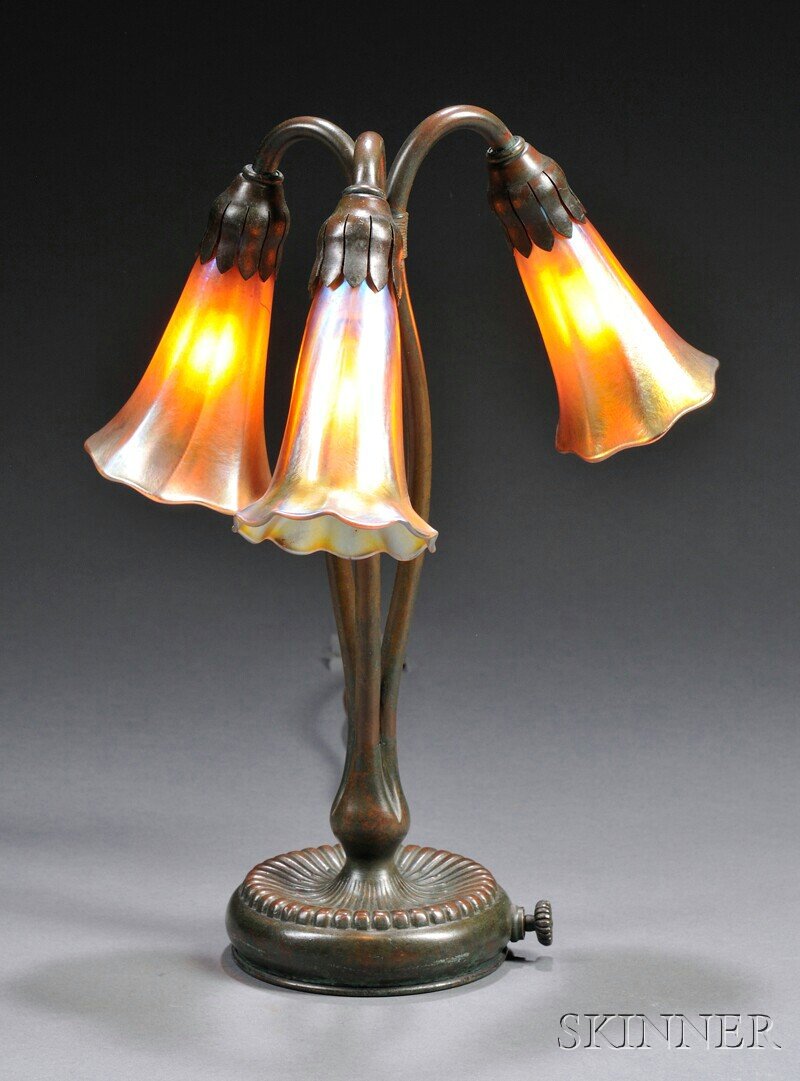 , Tiffany Studios Lily Lamp, Bronze and art glass,: Tiffany Studios Lily Lamp Bronze and art glass New York, early 20th century Three gold favrile lily-form shades pendant from tri-form standard raised on ribbed base in verdigris patina, base marked Ti