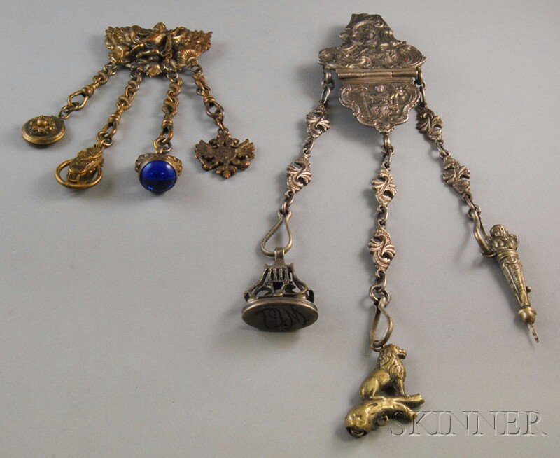 Two Lady's Chatelaines, a Leo Glass costume jewelr: Two Lady's Chatelaines, a Leo Glass costume jewelry chatelaine-type brooch of a repousse cherub hung with a small locket, a blue glass fob, and a heraldry-type motif, and a G. Accarisi Firenze cast si